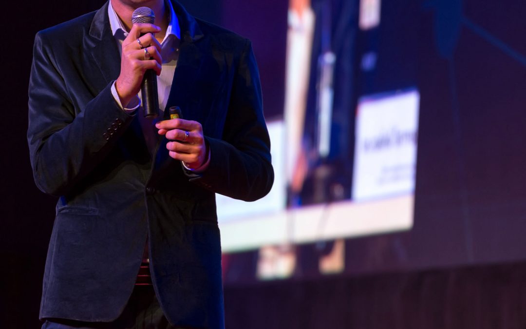 male public speaker holding a microphone, face not visible