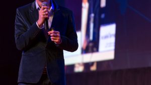 male public speaker holding a microphone, face not visible